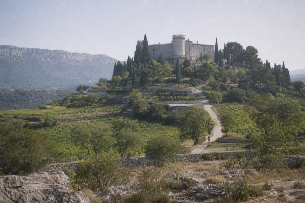 A stone château with cypress trees and vineyards on a Provençal hillside, no text, no logos, no people