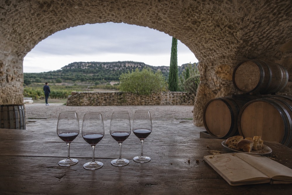 Glasses of red wine lined up on a wooden tasting table in a Provençal cellar, no text, no logos, no people.