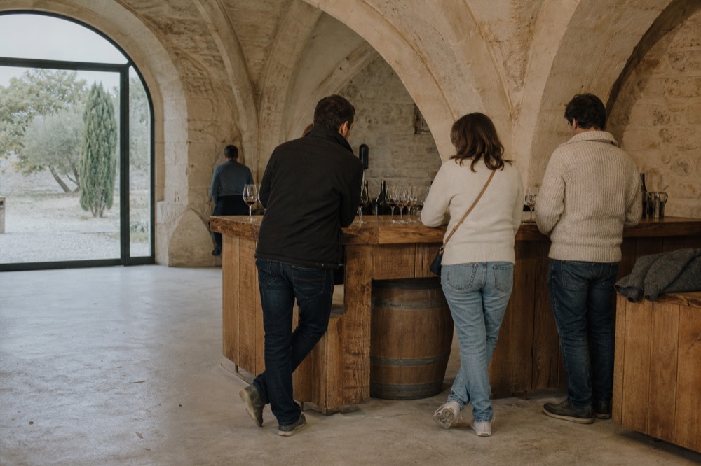 Casually dressed visitors standing at a wooden tasting bar inside a stone cellar, no text, no logos, no people
