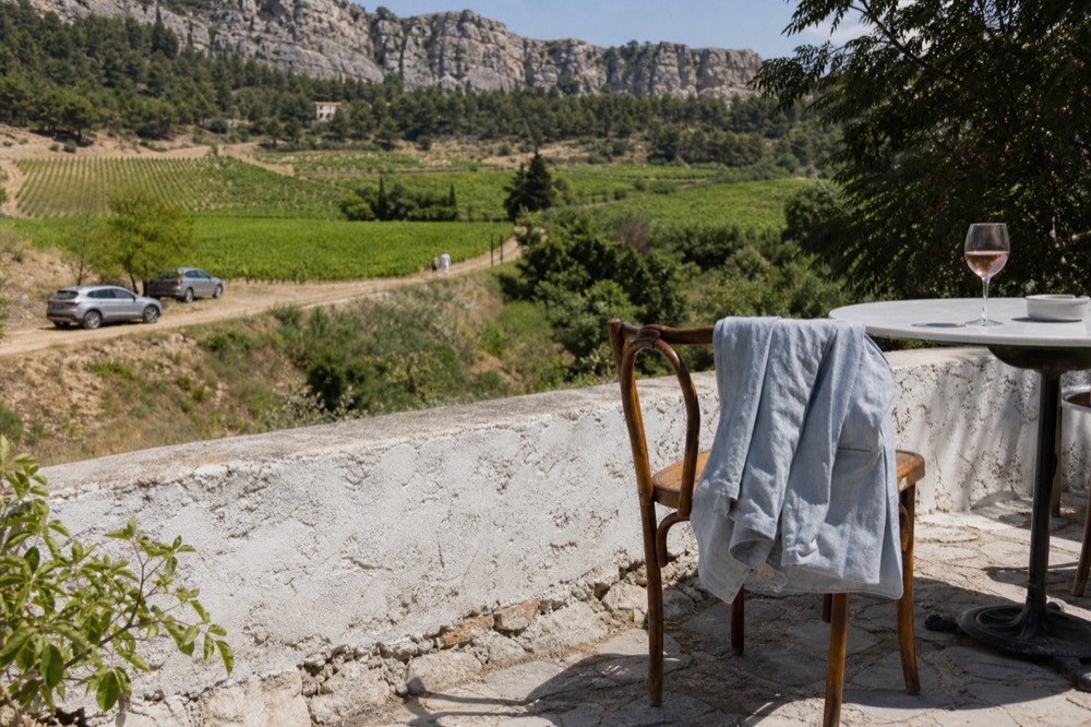 Sunlit terrace with vineyard view and a light jacket draped over a chair at a wine estate, no text, no logos, no people