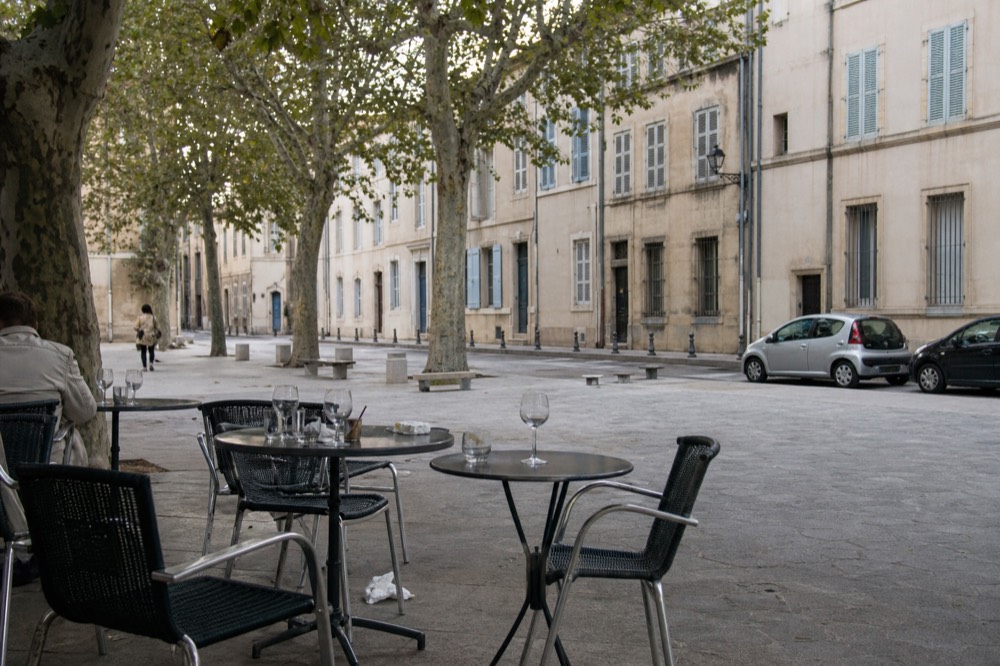 A stone square in Avignon's old town with café tables and shuttered facades, no text, no logos, no people.