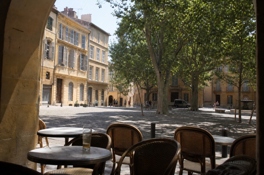 A café terrace on a sunlit square in Aix-en-Provence's old town, no text, no logos, no people.