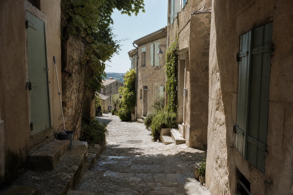 Narrow stone street in a Luberon hilltop village with shuttered houses, no text, no logos, no people.