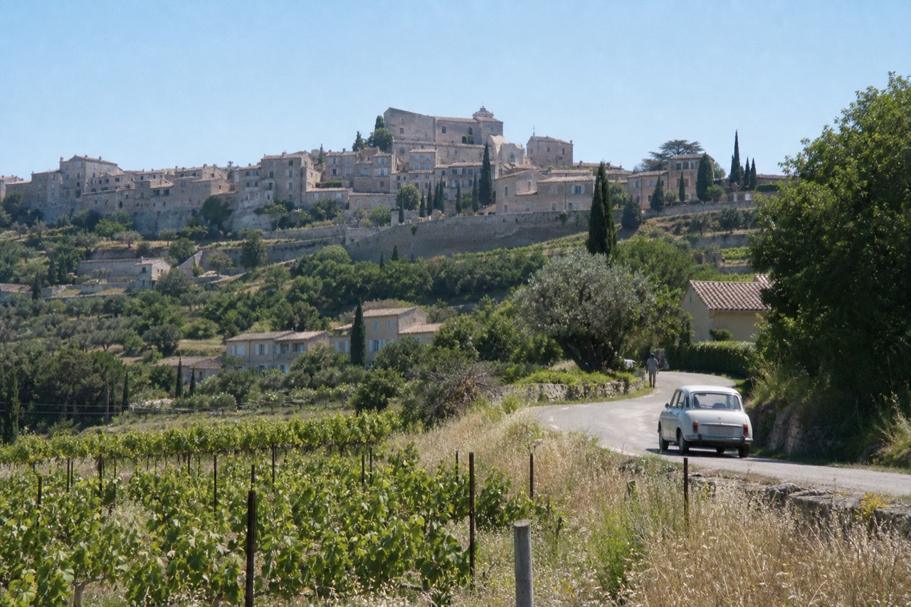 A hilltop Provence village with stone houses and cypress trees under clear sky, no text, no logos, no people.