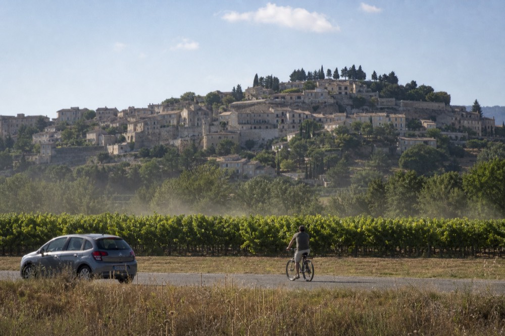 Vineyards stretching toward a hilltop village under a bright sky, no text, no logos, no people