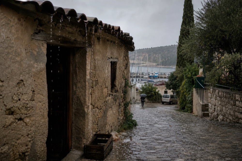 Rain-wet cobblestones outside a stone cellar building in a Provençal village, no text, no logos, no people