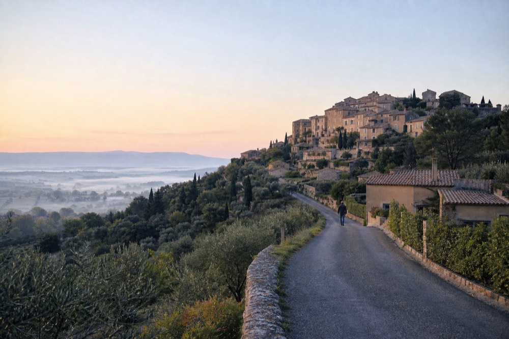 A hilltop village above vineyards and olive groves in the Luberon under a wide sky, no text, no logos, no people